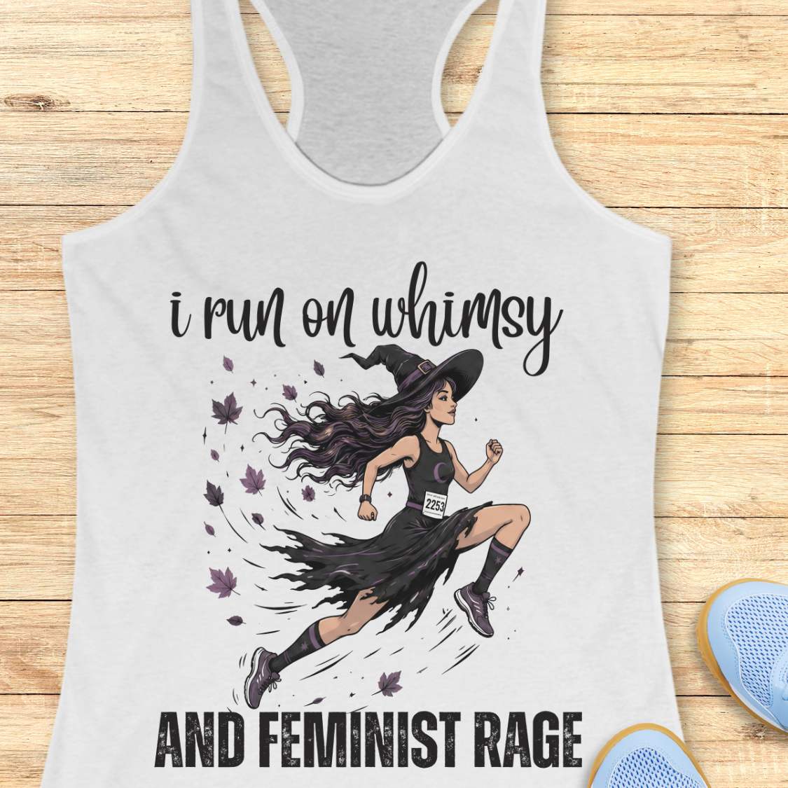 white tank top with a graphic of a witch runner and text  i run on whimsy and feminist rage, on a wooden surface