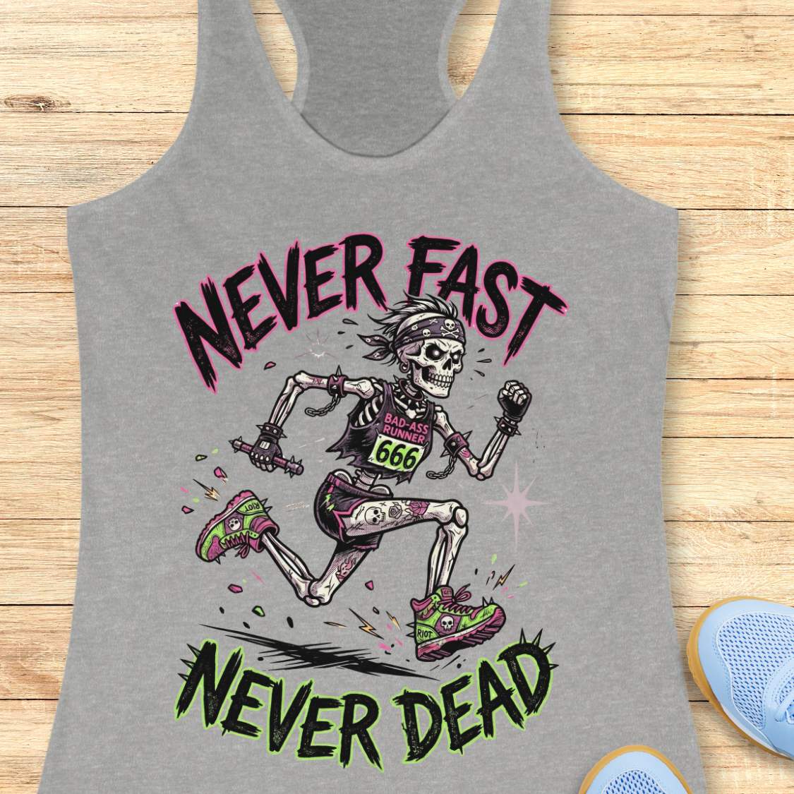 Gray tank top with skeleton running design and text 'Never Fast Never Dead' on a wooden surface.