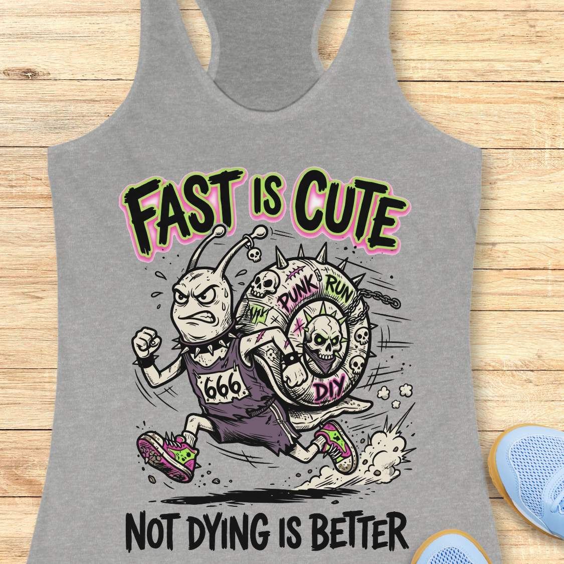 Gray tank top with a graphic design featuring cartoon characters and text fast is cute not dying is better, on a wooden surface.