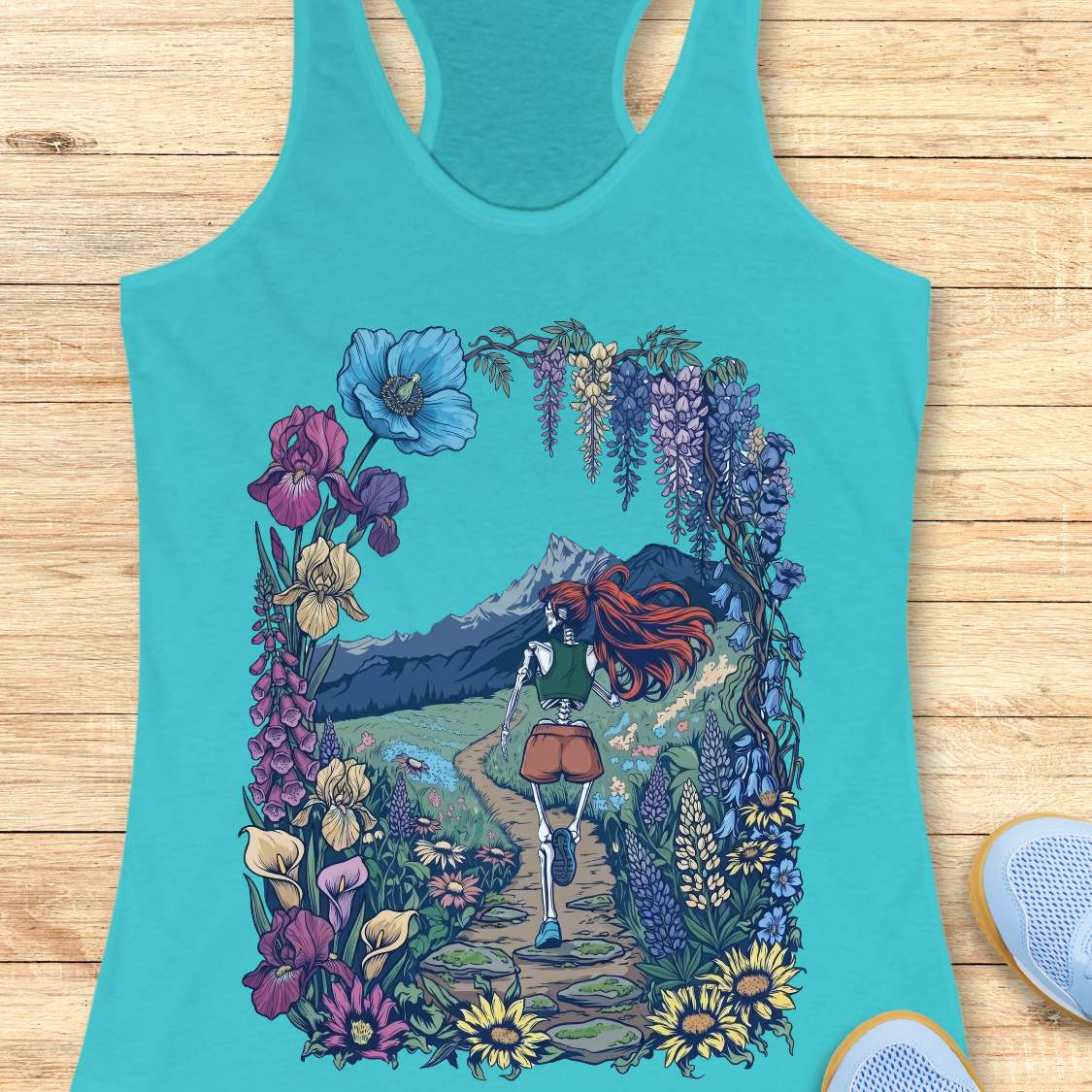 Turquoise tank top with a colorful graphic of a person with red hair and flowers on a wooden surface
