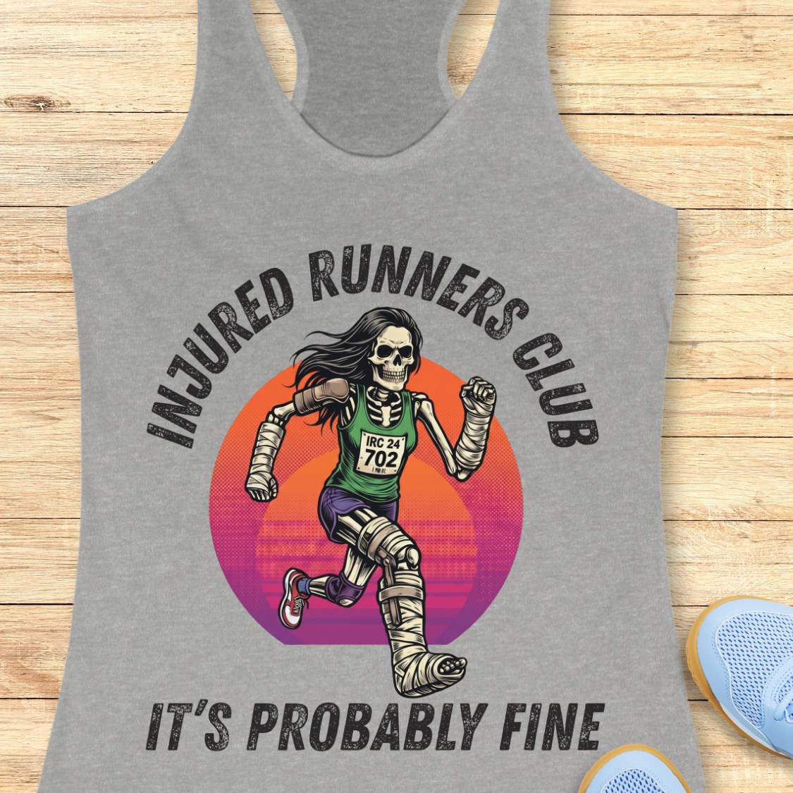 Gray tank top with skeleton runner graphic and 'Injured Runners Club' text on a wooden surface