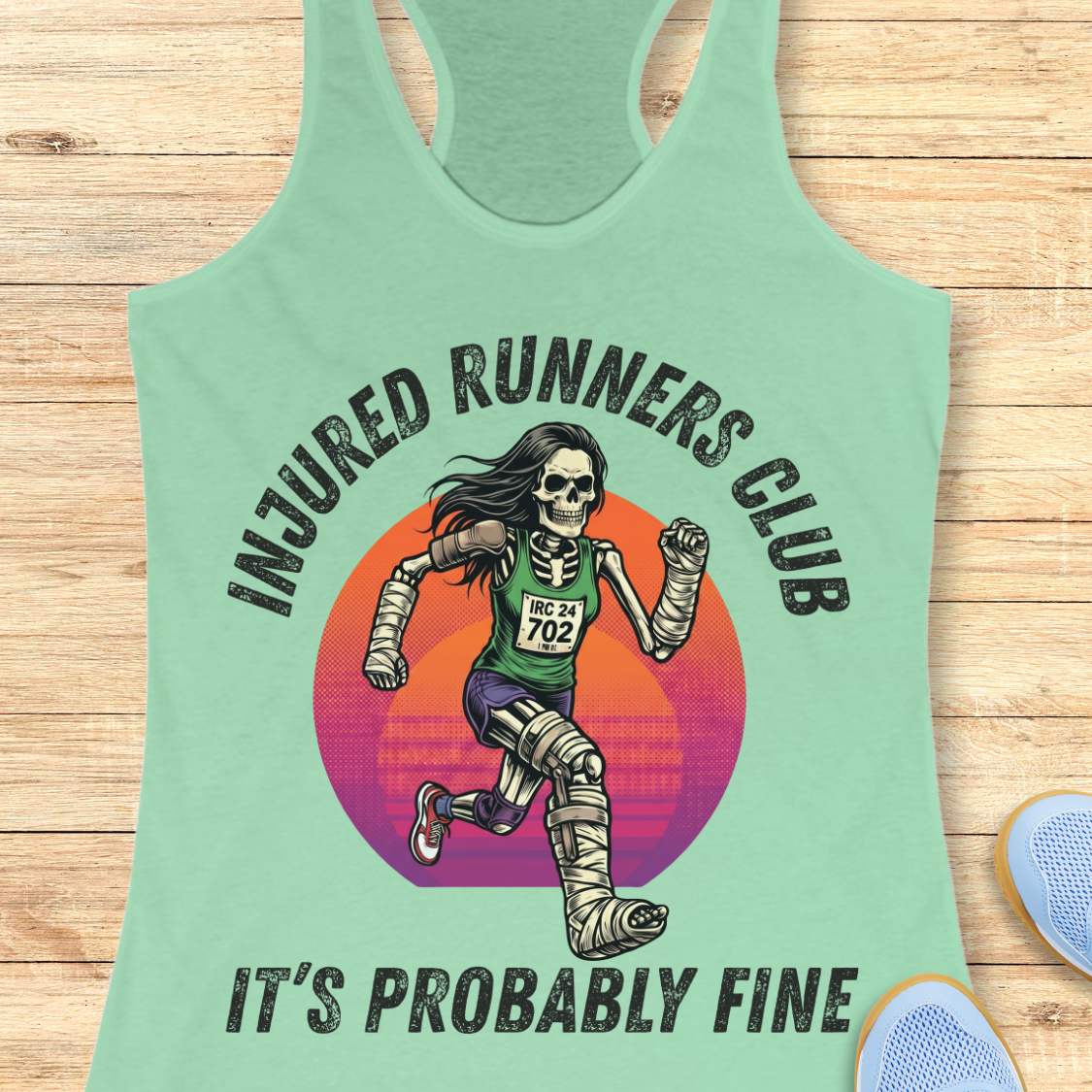 Light green tank top with 'Injured Runners Club' graphic on a wooden surface