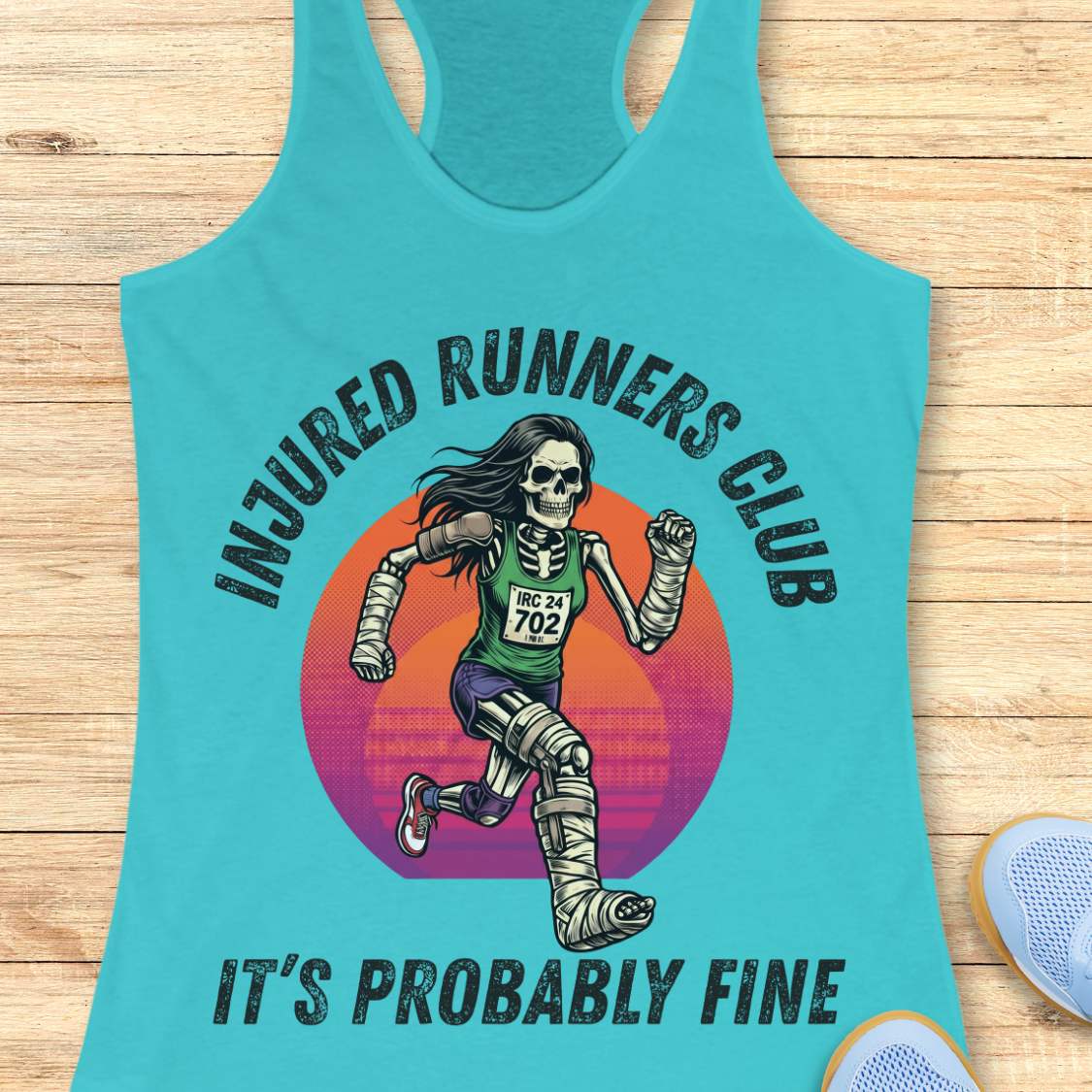 Turquoise tank top with skeleton runner graphic and text injured runners club, it's probably fine, on a wooden surface