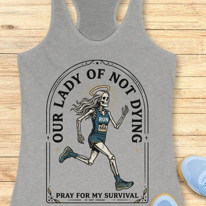 Gray tank top with skeleton runner design and text Our lady of noy dying, pray for my survival, on a wooden surface