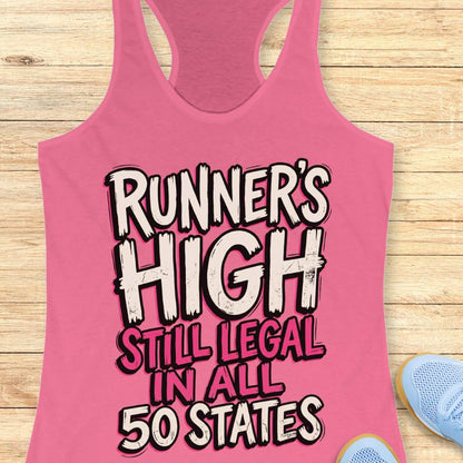 Pink tank top with 'RUNNER'S HIGH STILL LEGAL IN ALL 50 STATES' text on a wooden surface.