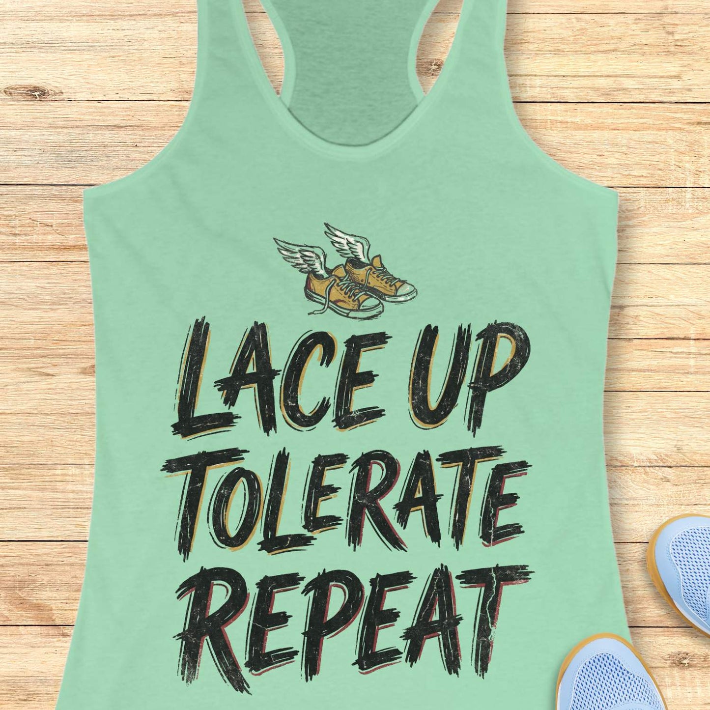 Light green tank top with text 'Lace Up Tolerate Repeat' on a wooden surface.