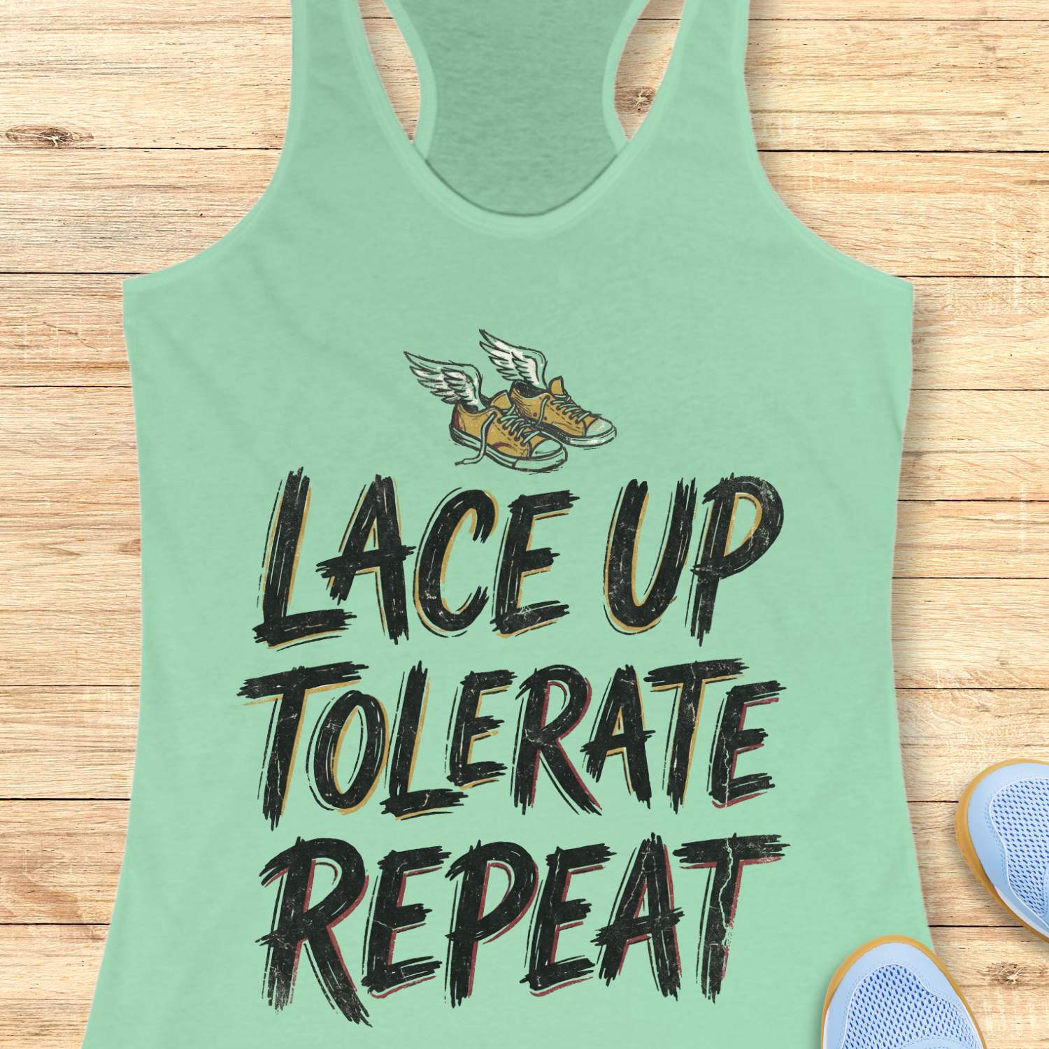 Light green tank top with text 'Lace Up Tolerate Repeat' on a wooden surface.