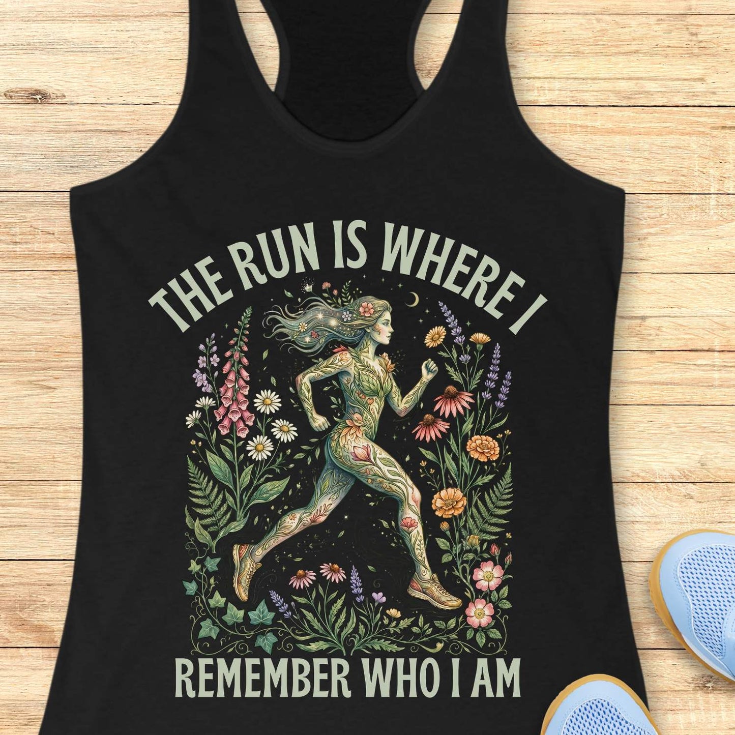 Black tank top with a graphic design of a woman running among flowers and text The run is where I remember who I am , on a wooden surface.