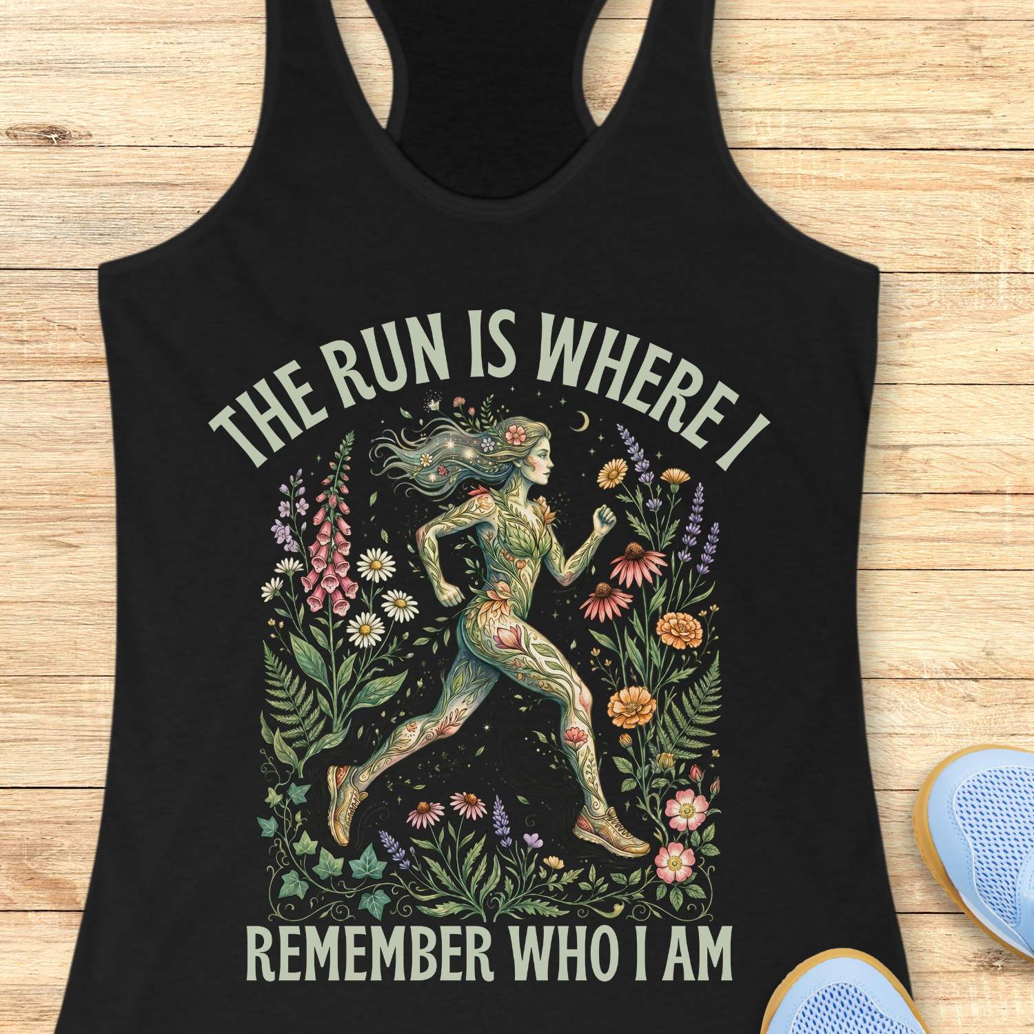 Black tank top with a graphic design of a woman running among flowers and text The run is where I remember who I am , on a wooden surface.