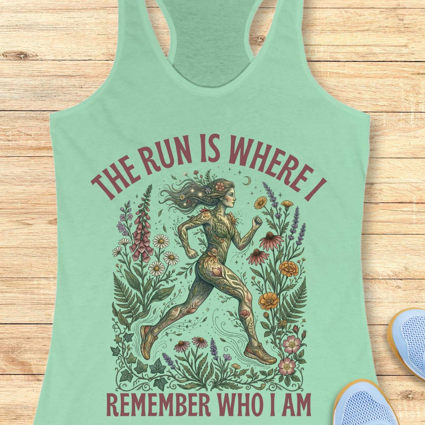 Mint green tank top with a graphic design of a runner surrounded by nature and text The run is where I remember who I am , on a wooden surface.