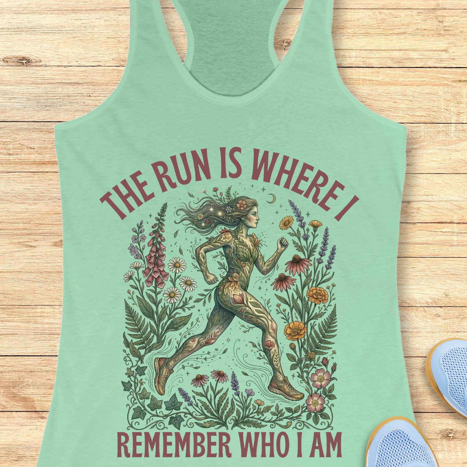 Mint green tank top with a graphic design of a runner surrounded by nature and text The run is where I remember who I am , on a wooden surface.