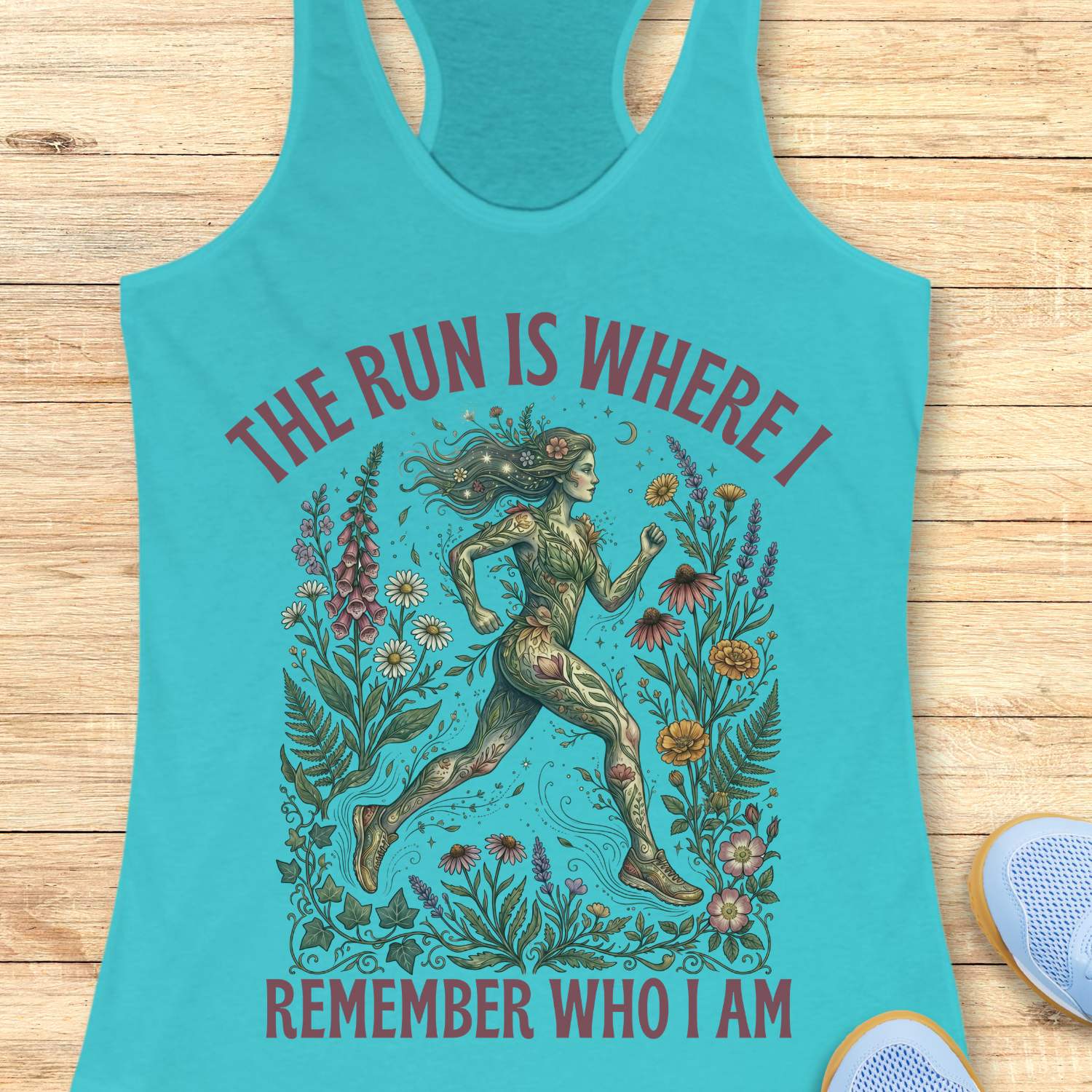 Turquoise tank top with a graphic of a woman running surrounded by nature and text The run is where I remember who I am ,on a wooden surface.