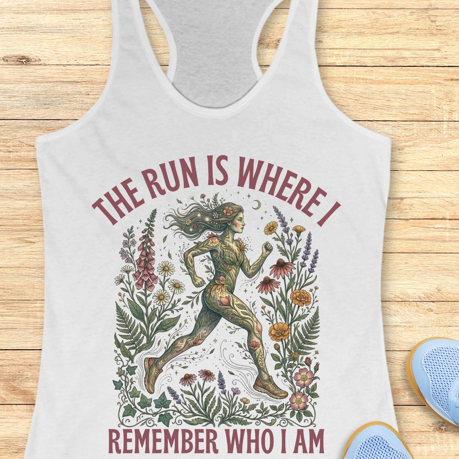 white Tank top with a graphic design of a woman running surrounded by nature and text - The run is where I remember who I am , on a wooden surface.