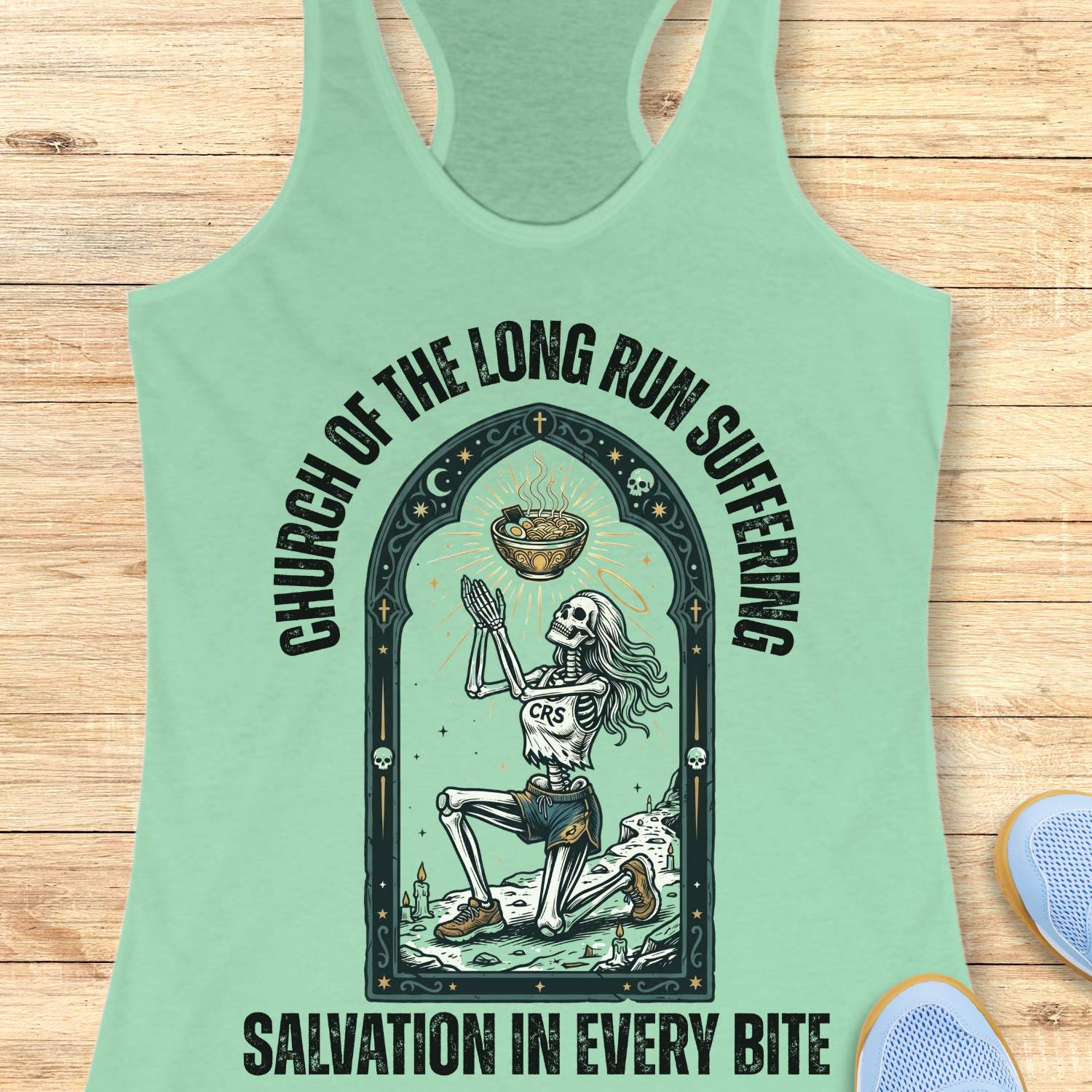 Mint green tank top with skeleton design and text 'Church of the long run suffering. Salvation in every bite', on a wooden surface
