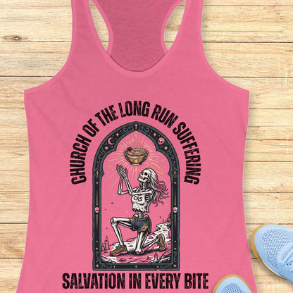 Pink tank top with skeleton design and text 'Church of the long run suffering. Salvation in every bite', on a wooden surface