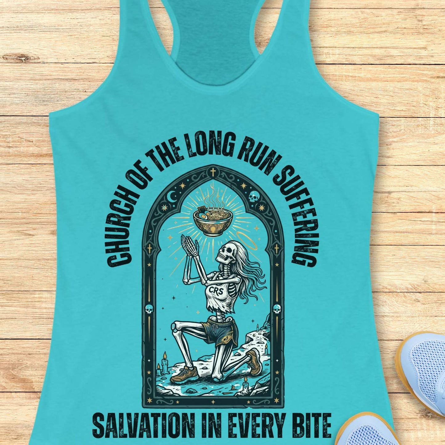 Turquoise tank top with skeleton design and text 'Church of the long run suffering. Salvation in every bite', on a wooden surface