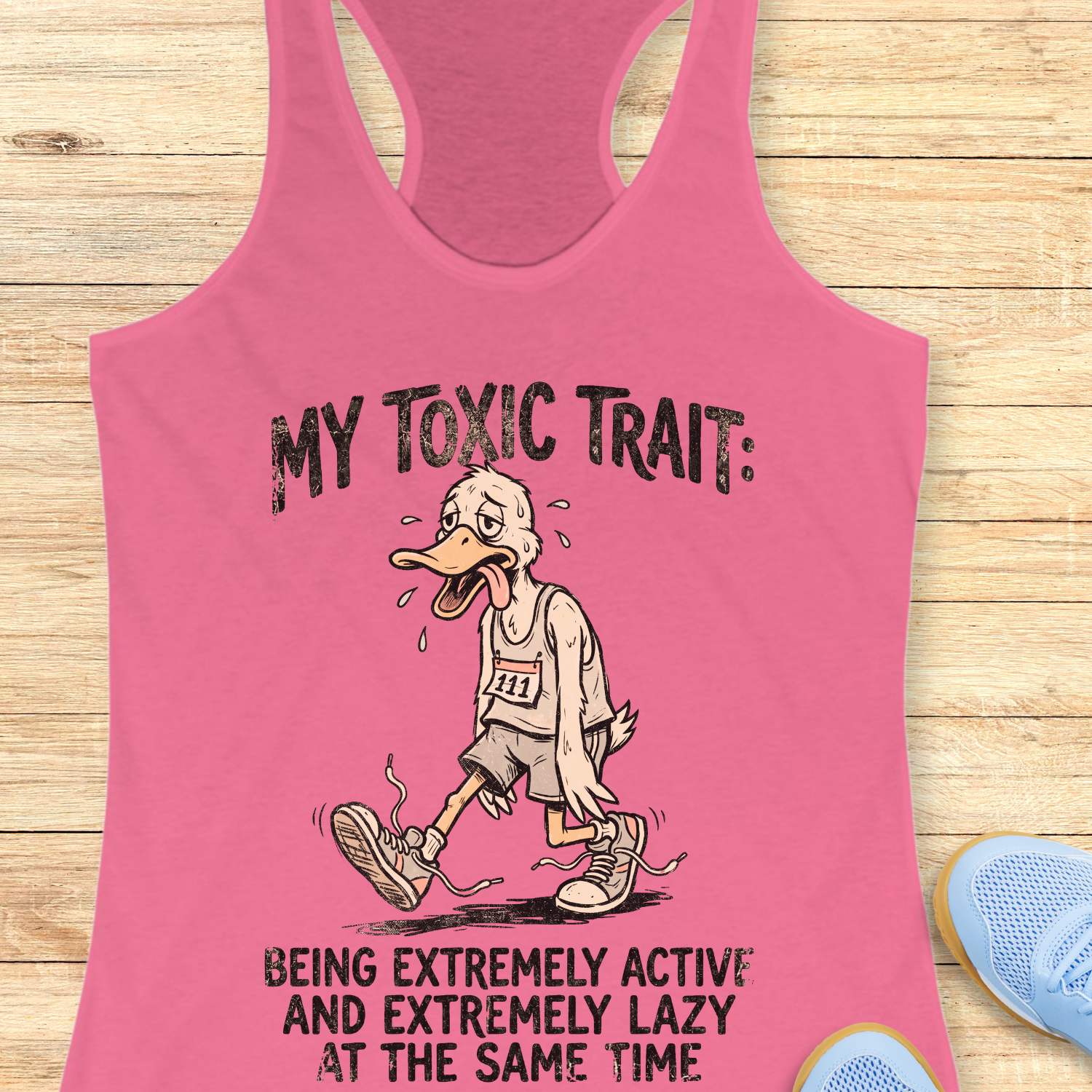 Pink tank top with cartoon character and humorous text ' my toxic trait - being extremely active and extremely lazy at the same time',  on a wooden surface