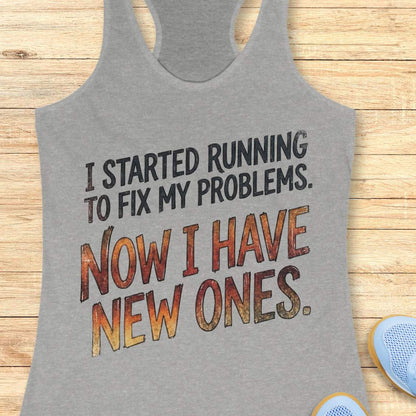 Gray tank top with humorous text 'I started running to fix my problems. Now I have new ones.' on a wooden surface