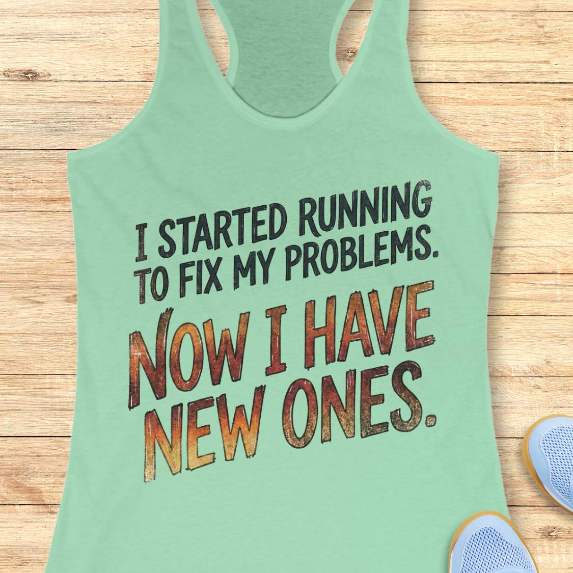 Mint green tank top with humorous text 'I started running to fix my problems. Now I have new ones.' on a wooden surface
