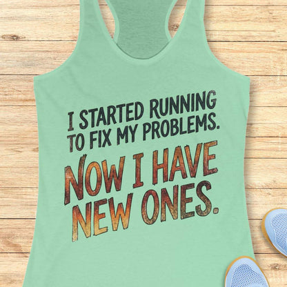 Mint green tank top with humorous text 'I started running to fix my problems. Now I have new ones.' on a wooden surface