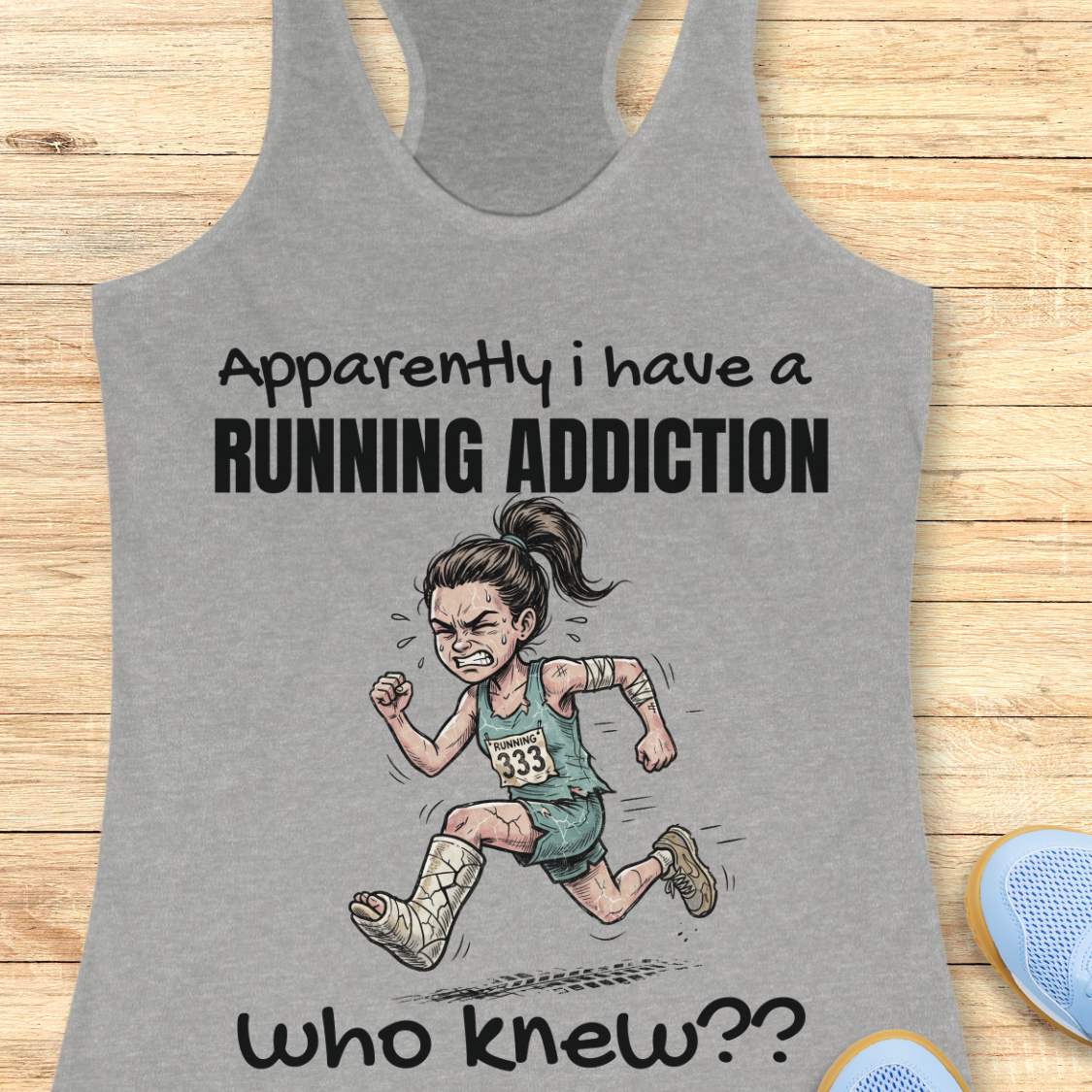 Gray tank top with a graphic of a running person and text  'apparently I have a running addiction. who knew??'  on a wooden surface