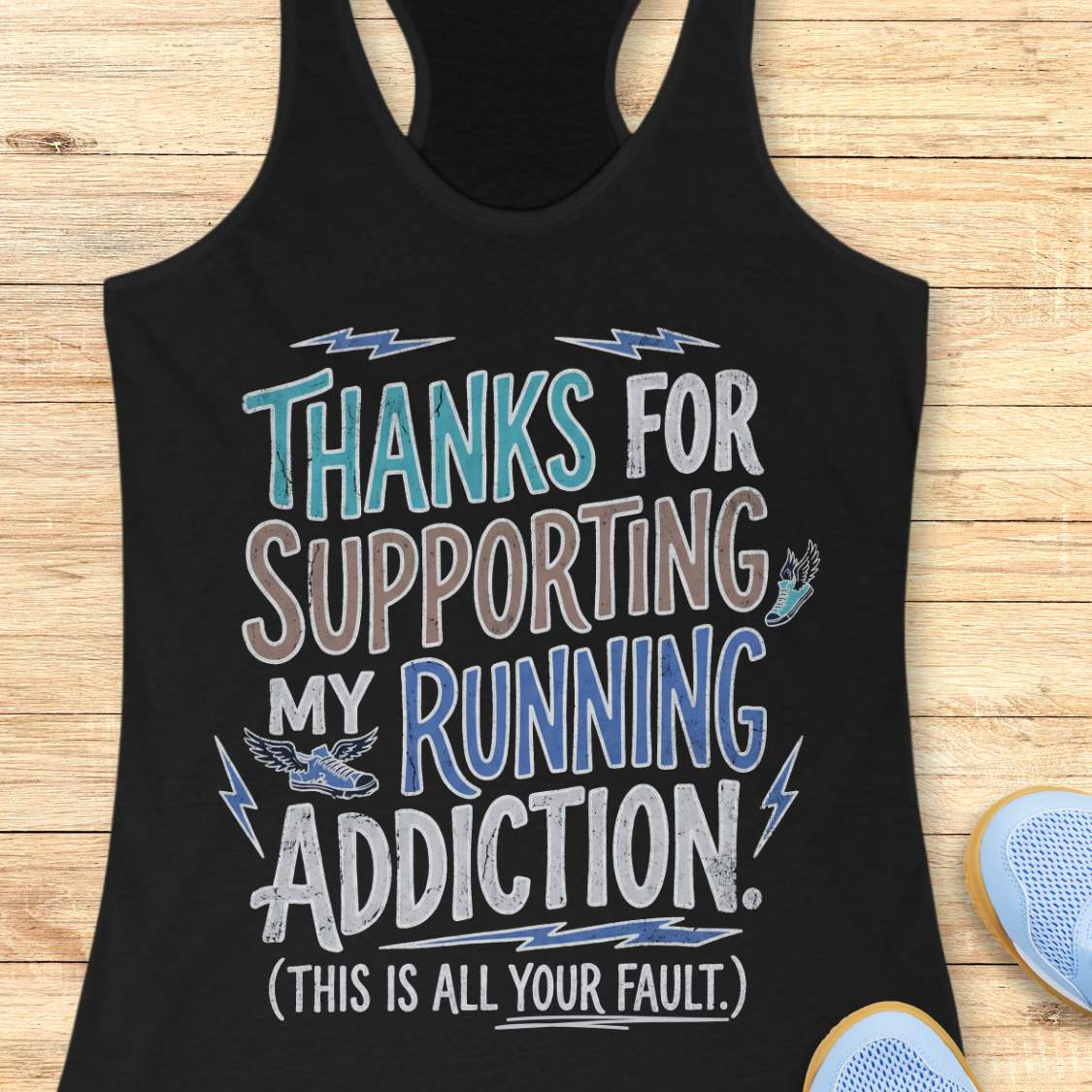 Black tank top with humorous text 'thanks for supporting my running addiction. (This is all your fault.)' design on a wooden surface