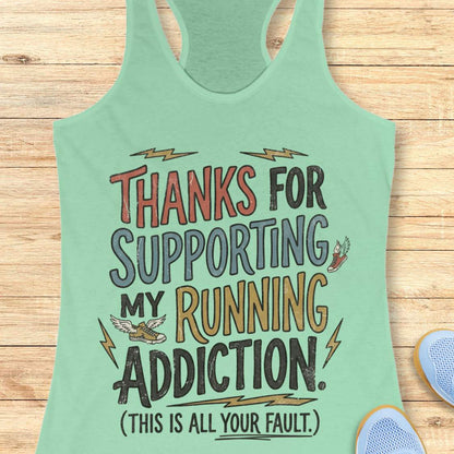 Mint green tank top with humorous text 'thanks for supporting my running addiction. (This is all your fault.)'  on a wooden surface