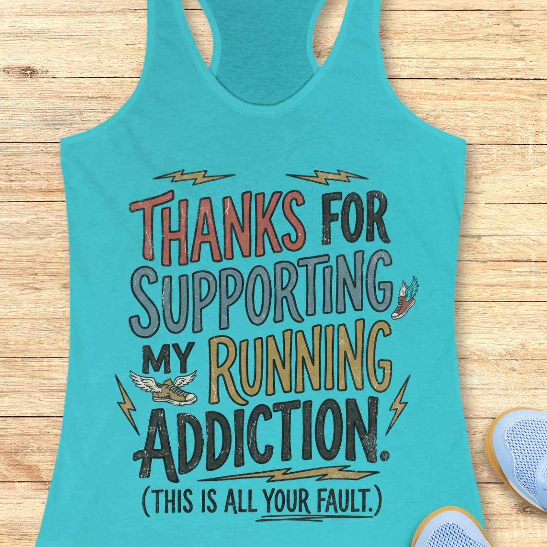 Turquoise tank top with humorous text 'thanks for supporting my running addiction. (This is all your fault.)' on a wooden surface