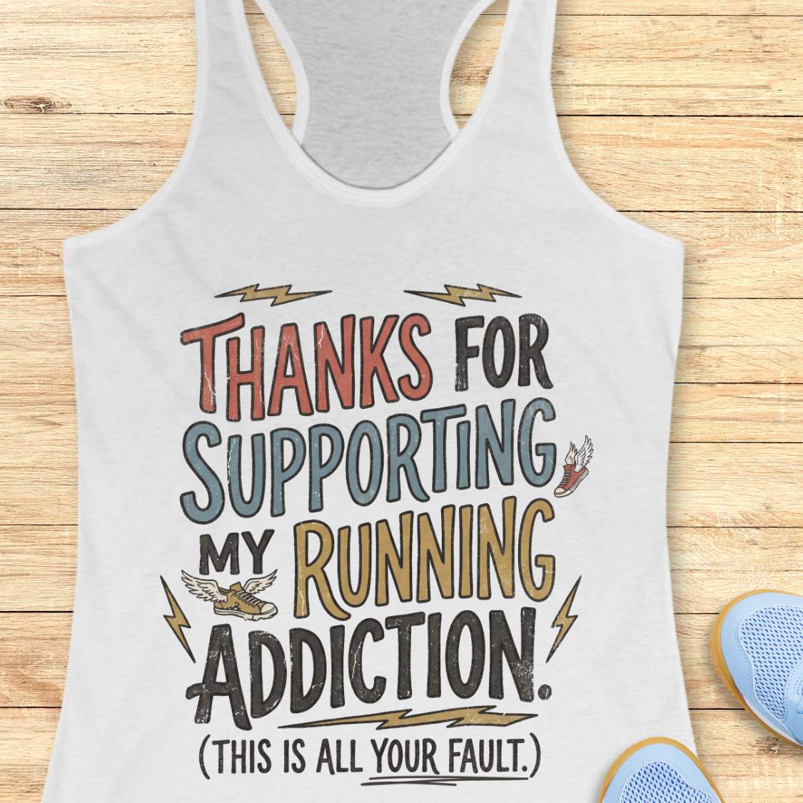 white tank top with colorful text 'thanks for supporting my running addiction. (This is all your fault.)'  on a wooden surface