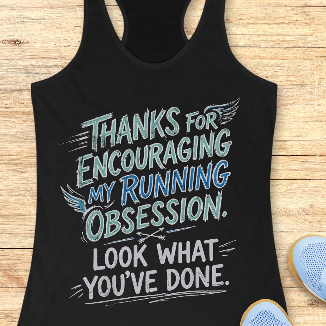 Black tank top with motivational text 'Thanks for encouraging my running obsession. Look what you've done.' on a wooden surface