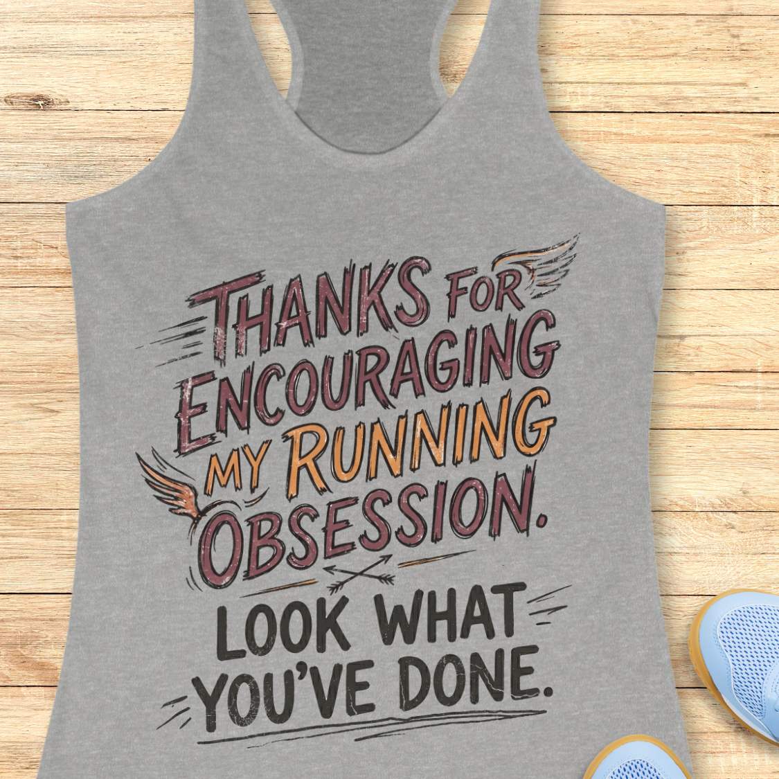 Gray tank top with motivational text 'Thanks for encouraging my running obsession. Look what you've done.' on a wooden surface