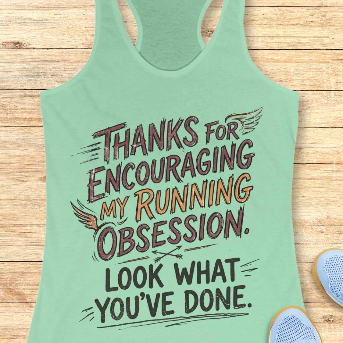 Green tank top with motivational text 'Thanks for encouraging my running obsession. Look what you've done.' on a wooden surface