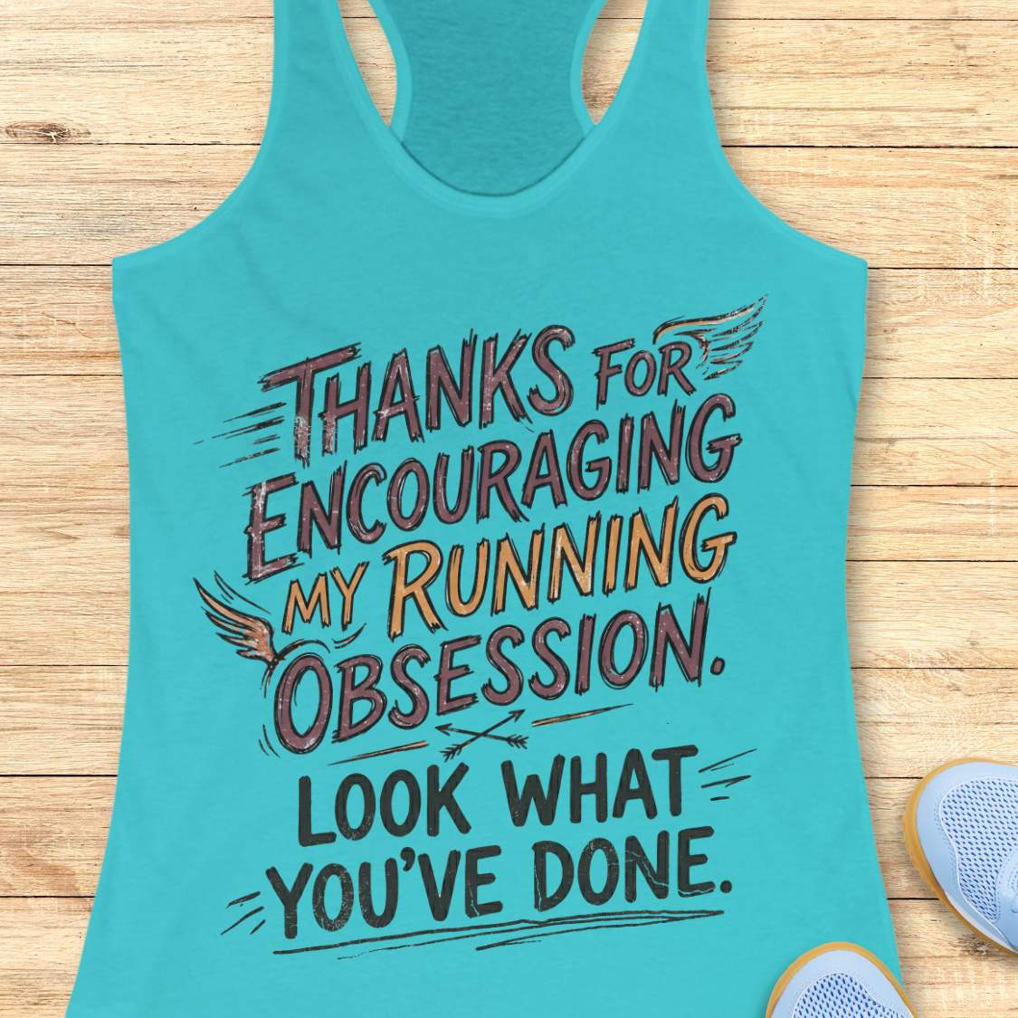 Turquoise tank top with motivational text  'Thanks for encouraging my running obsession. Look what you've done.' on a wooden surface