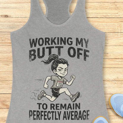 Gray tank top with a graphic of a runner and text  'working my butt off to remain perfectly average', on a wooden surface