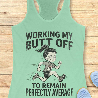 Mint green tank top with a graphic and text  'working my butt off to remain perfectly average', on a wooden surface