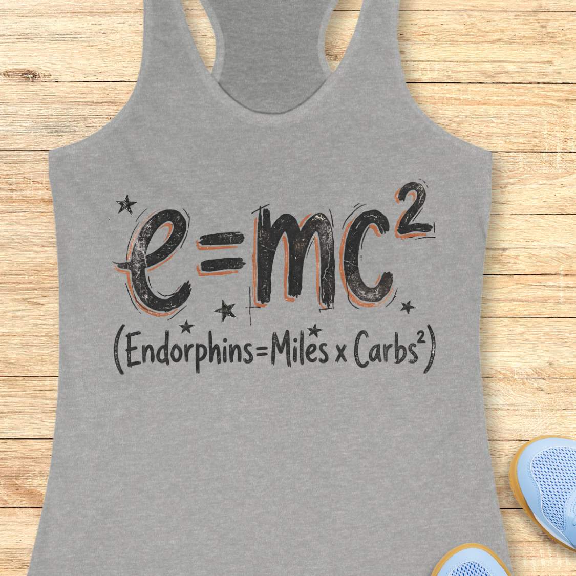 Gray tank top with a humorous equation printed on it, with text - 'Endorphins = Miles X Carbs square' placed on a wooden surface.