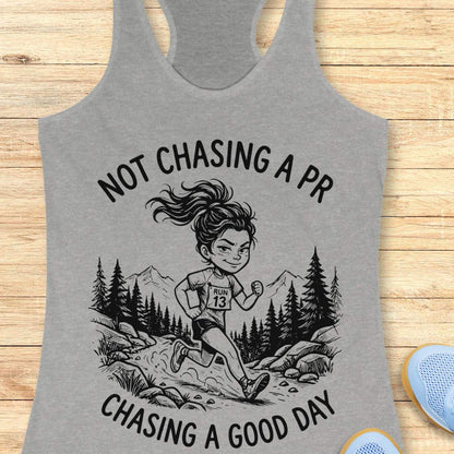 Gray tank top with a graphic of a runner and text 'Not Chasing A PR, Chasing A Good Day' on a wooden surface.