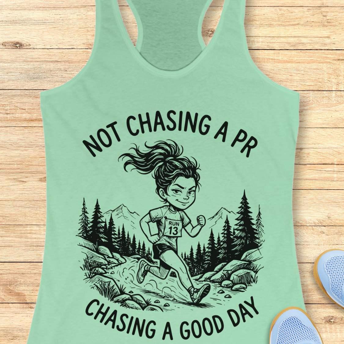 Mint green tank top with running graphic and text 'not chasing a PR, chasing a good day', on a wooden surface