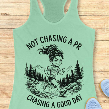 Mint green tank top with running graphic and text 'not chasing a PR, chasing a good day', on a wooden surface