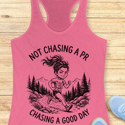Pink tank top with a graphic of a runner and text 'Not chasing a PR, chasing a good day' on a wooden surface.