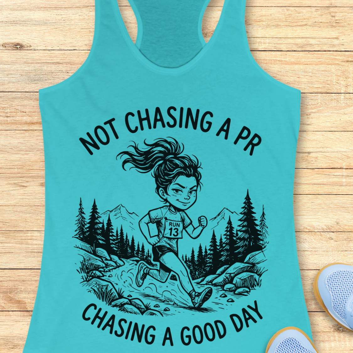 Turquoise tank top with running graphic and text 'not chasing a PR, chasing a good day', on a wooden surface