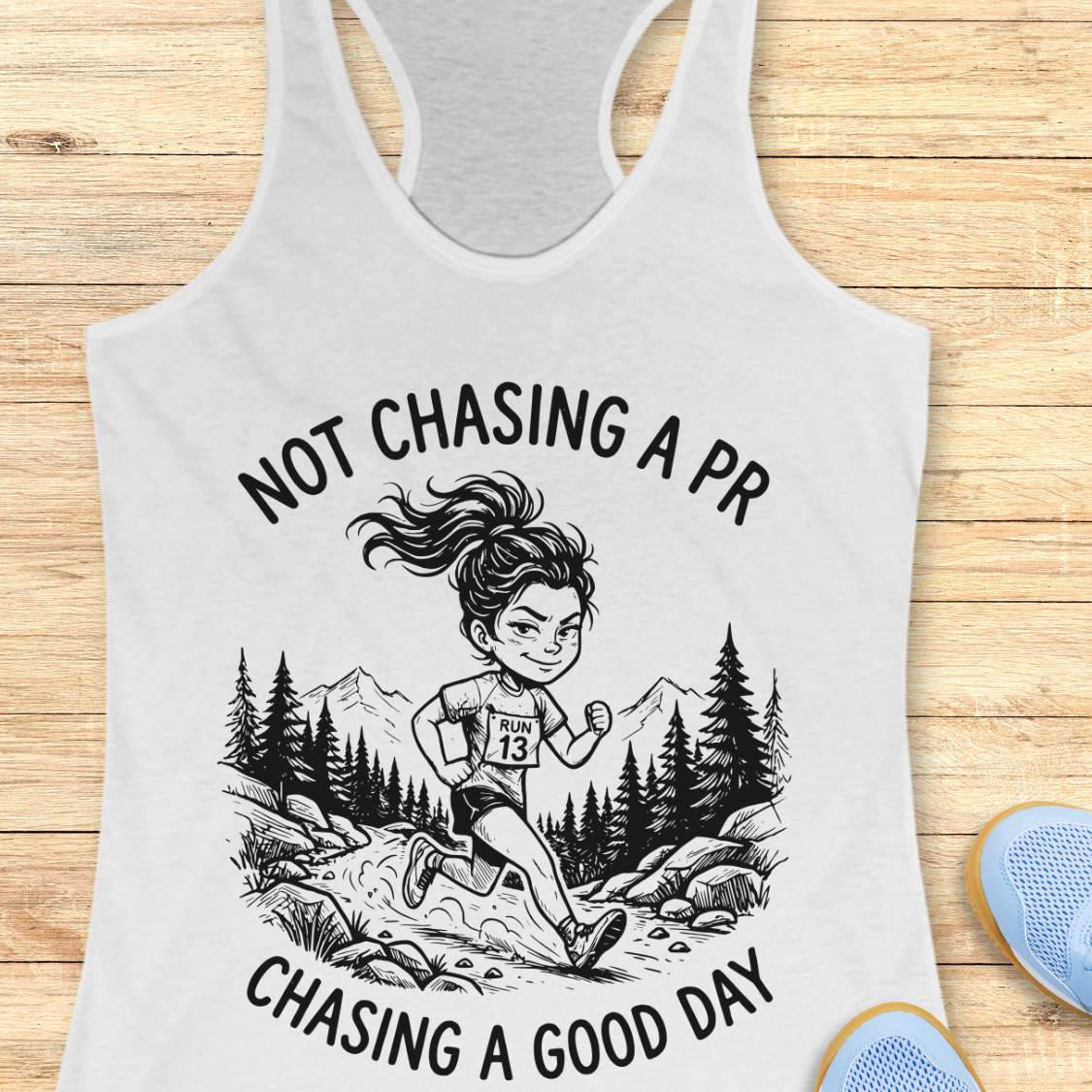 white tank top with a graphic of a runner and text 'Not Chasing a PR, Chasing a Good Day' on a wooden surface.