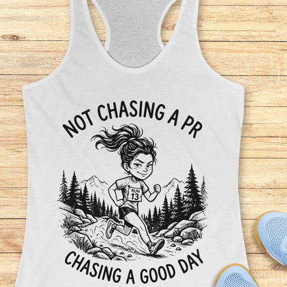 white tank top with a graphic of a runner and text 'Not Chasing a PR, Chasing a Good Day' on a wooden surface.