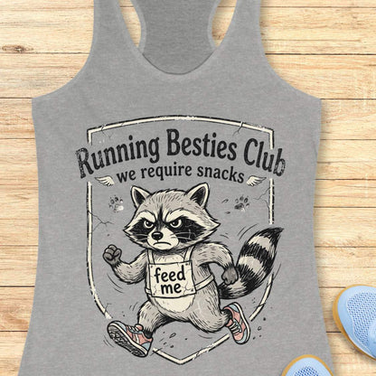 Gray tank top with raccoon graphic and 'Running Besties Club, we require snacks' text on a wooden surface
