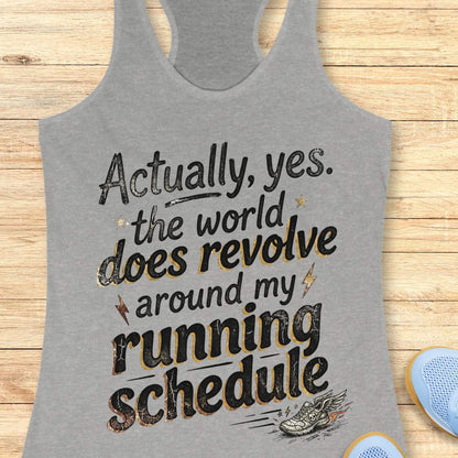 Gray tank top with funny text 'Actually, yes. the world does revolve around my running schedule.',  on a wooden surface