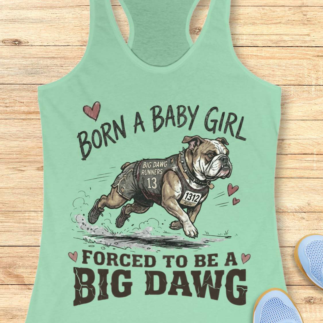 Light green tank top with bulldog graphic and text 'Born a baby girl forced to be a BIG DAWG', on a wooden surface
