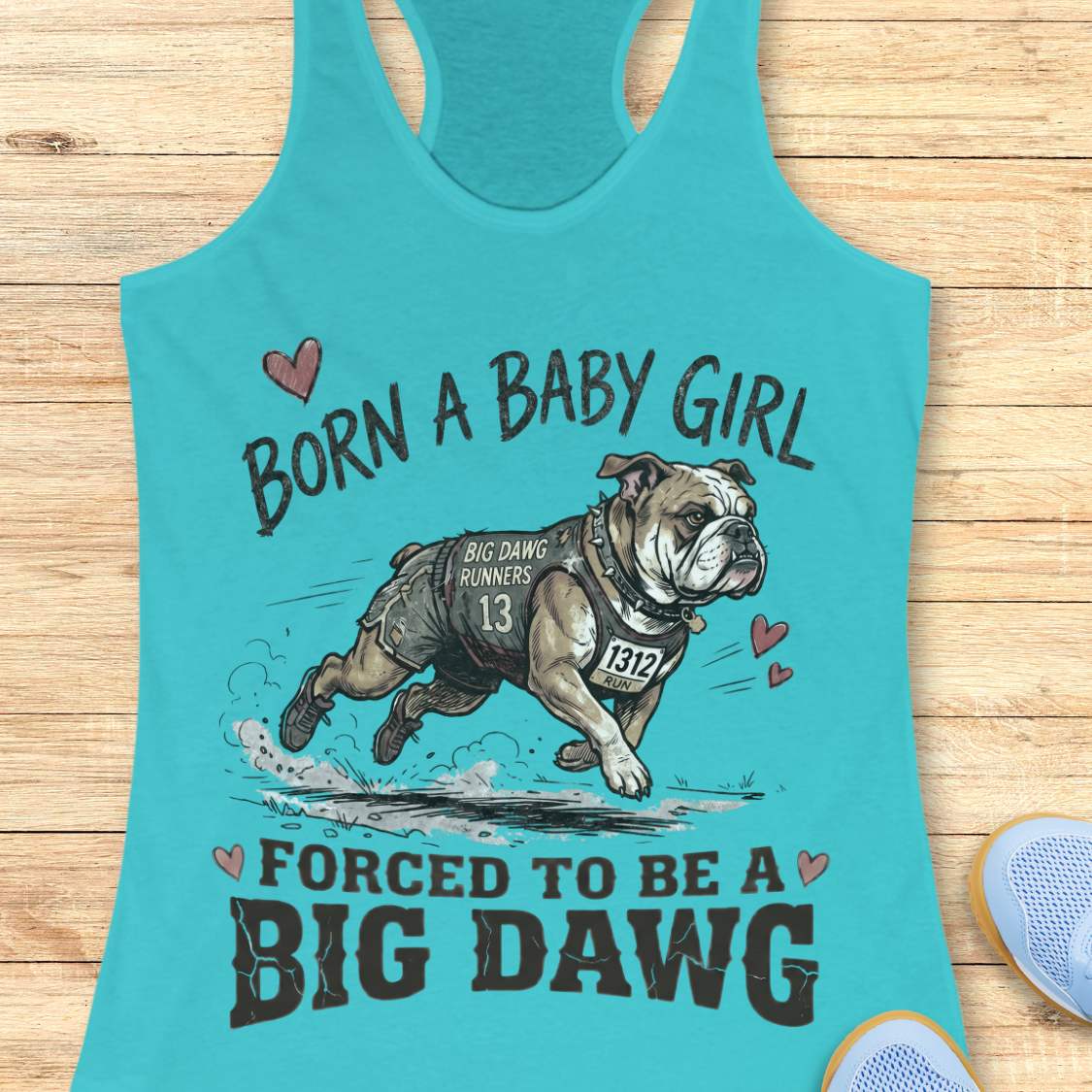Turquoise tank top with bulldog graphic and text 'Born a baby girl forced to be a BIG DAWG', on a wooden surface