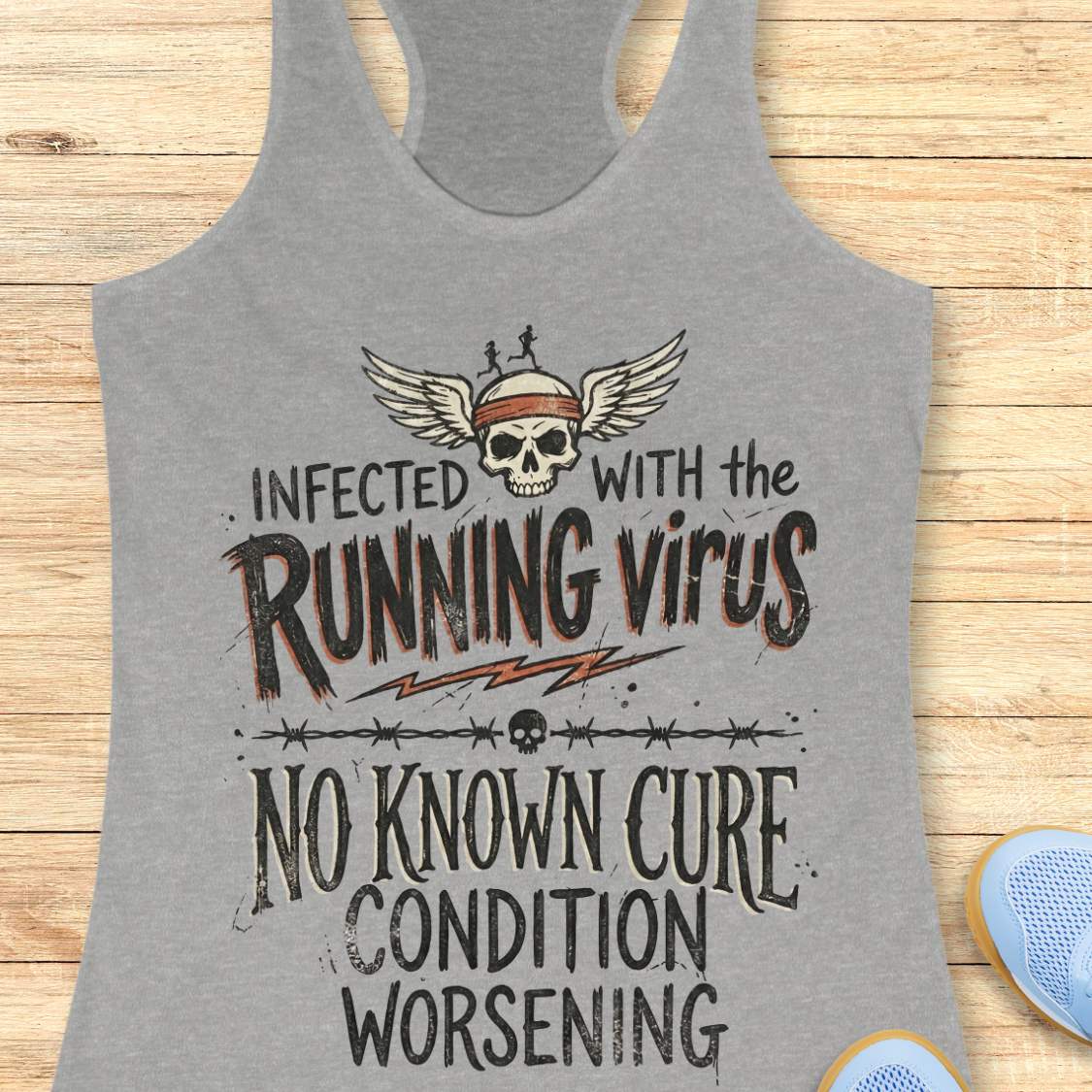 Gray tank top with graphic design and text 'infected with the running virus. No known cure, condition worsening', on a wooden surface
