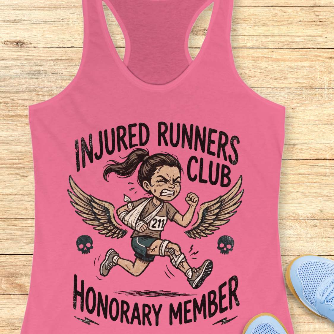 Pink tank top with 'Injured Runners Club Honorary Member' graphic on a wooden surface.