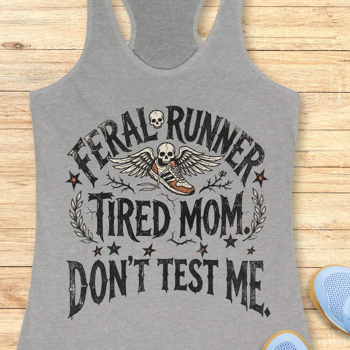 Gray tank top with 'Feral Runner Tired Mom Don't Test Me' text and graphic on a wooden surface.